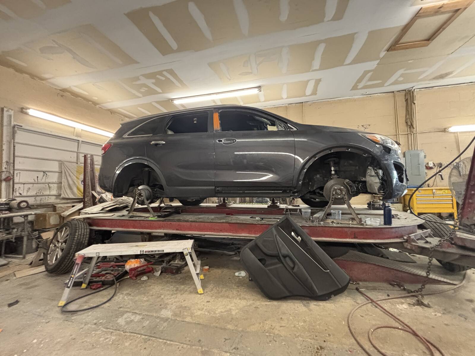 A gray SUV up on the frame rack at the shop with its wheels off.